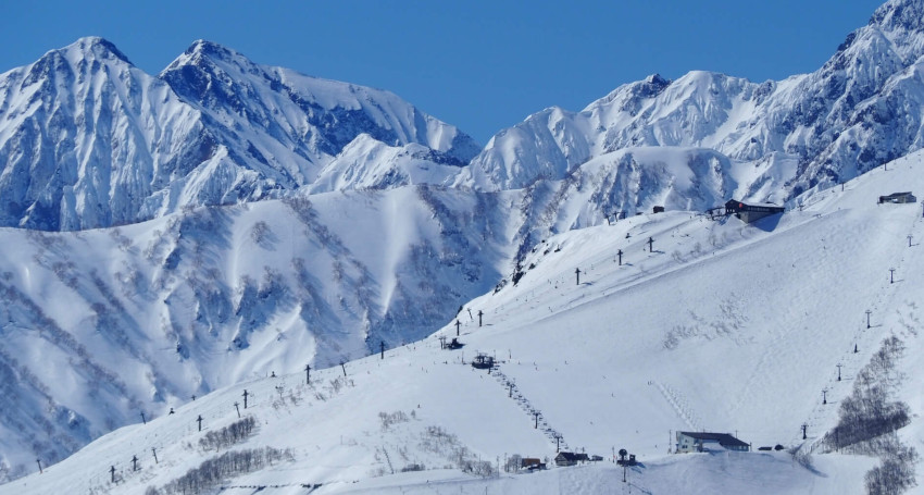 Snow-covered Happo One Hakuba, Japan mountains with ski lifts dotting the slopes under a clear blue sky.