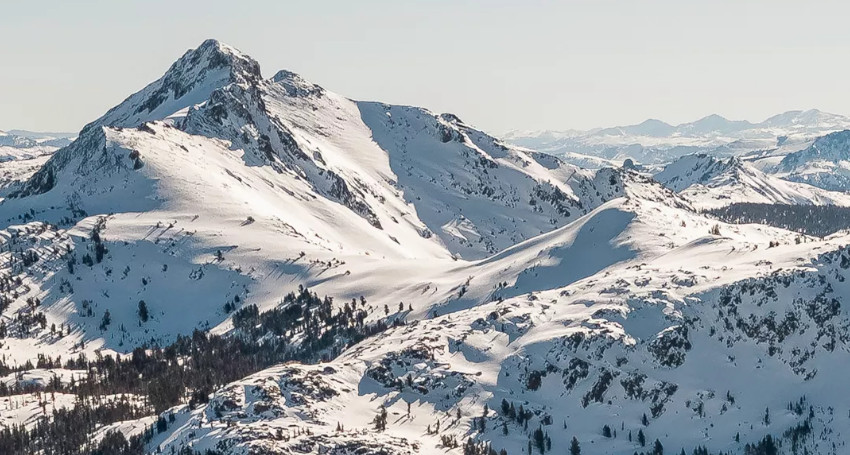 A snow-covered mountain range under a clear blue sky with scattered trees on the slopes at Kirkwood, California, USA