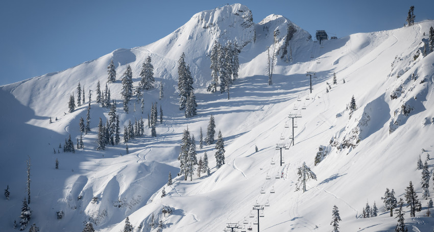 Snow-covered mountain in Palisades Tahoe, California with ski tracks, trees, and a ski lift on a clear day.