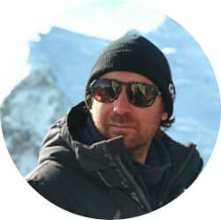 A person wearing dark sunglasses and a black beanie stands outdoors in a cold, snowy environment.