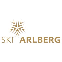 Logo of Ski Arlberg featuring a stylized snowflake design in gold on the left, with the words "Ski Arlberg" in gold lettering to the right of the snowflake.