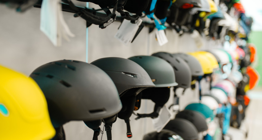 A display of various helmets, including black, yellow, and multicolored options perfect for skiing, arranged on racks against a wall.