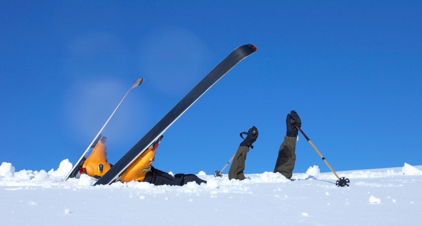 Two skiers lie on their backs in the snow with their skis and poles sticking up, set against a clear blue sky, enjoying a moment of rest after discovering how to prevent glasses from fogging in ski goggles.