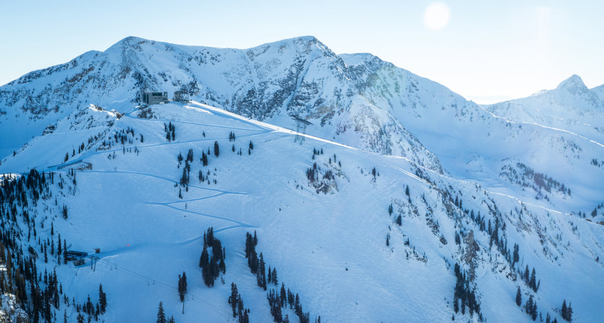 Snow-covered mountain landscape with ski tracks and a building at the peak under a clear sky at Snowbird, Utah, USA