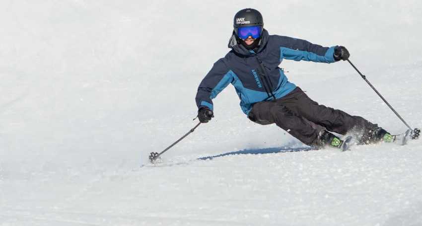 A person in blue and black skiing gear is skillfully carving downhill on a snowy slope, using ski poles for balance.
