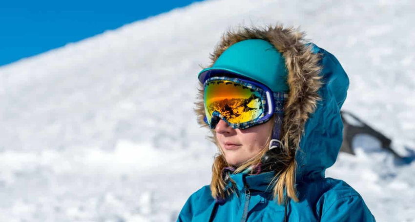 A person wearing a blue jacket, blue hat, and ski goggles stands in a snowy landscape.