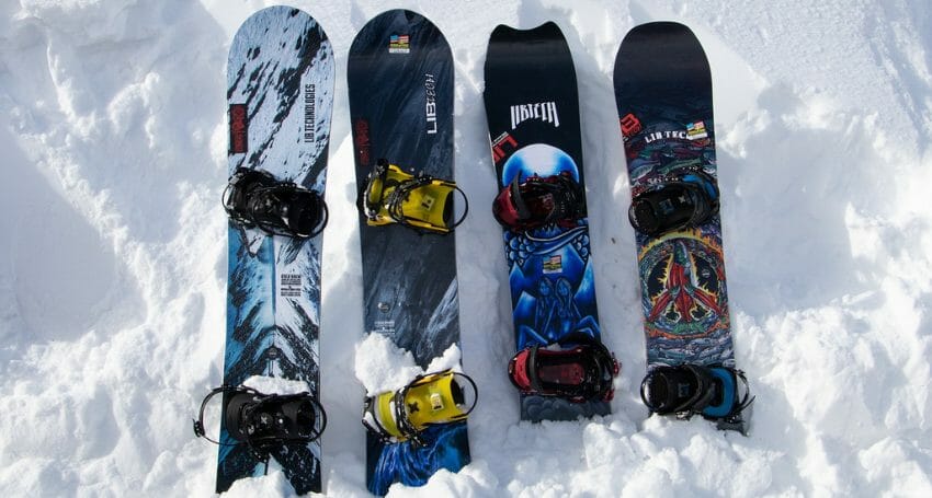 Four snowboards with attached bindings are placed upright in the snow, each featuring distinct designs and graphics.